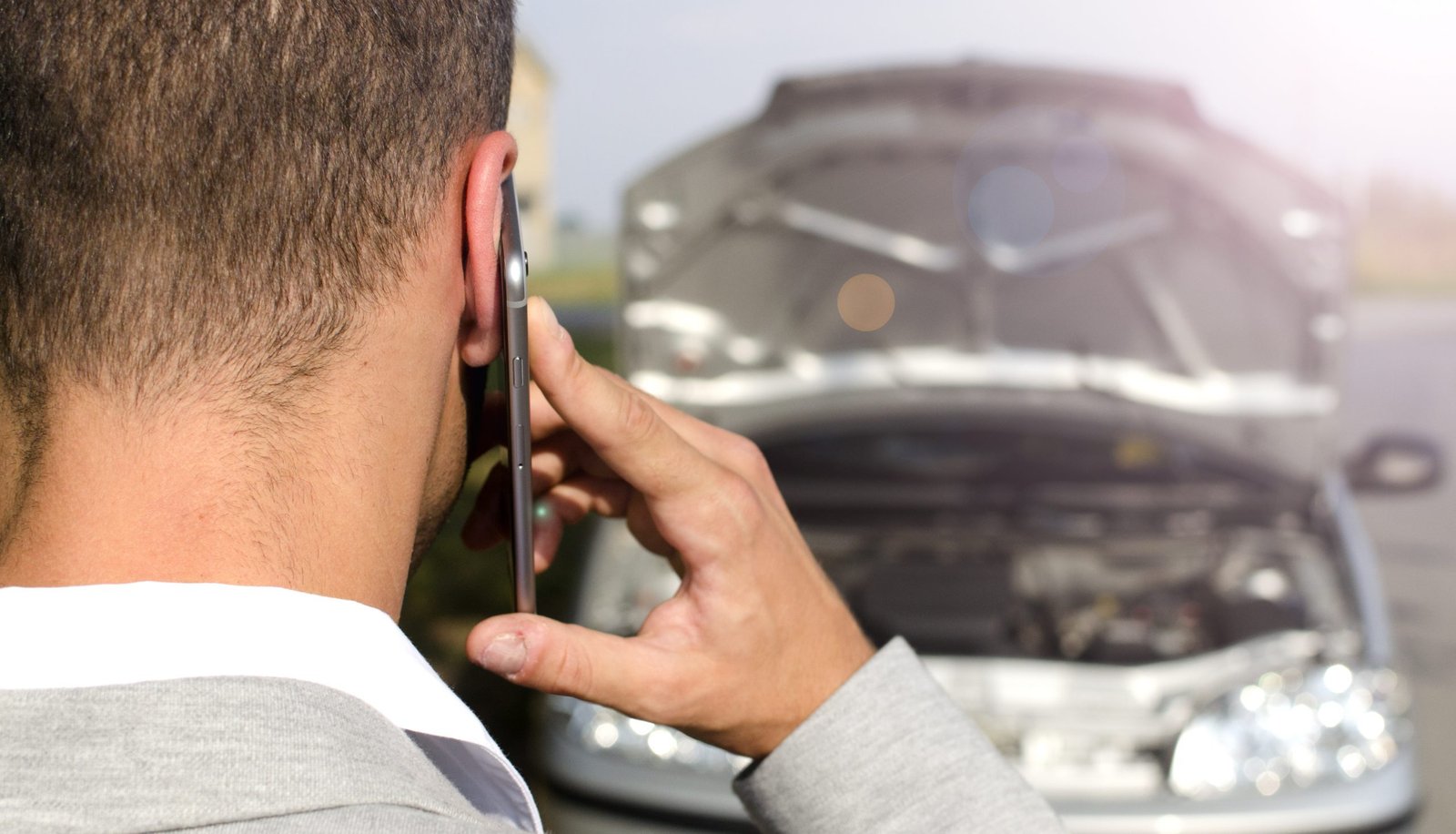 Man standing by the broken vehicle calls the insurance company.