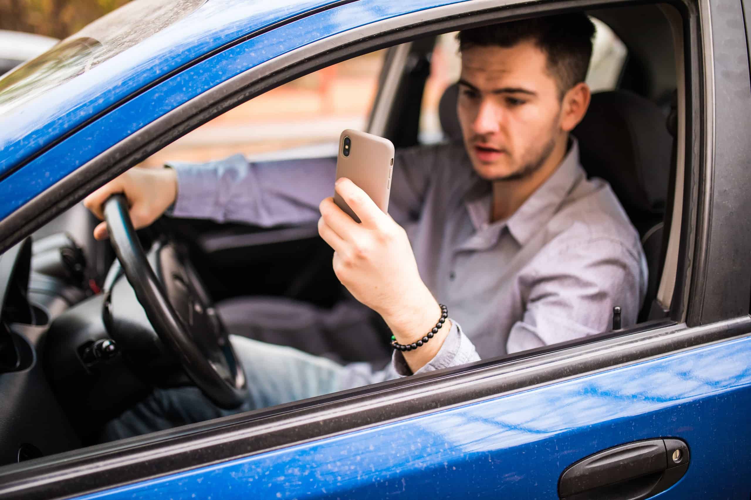 young man using cell phone while driving with one hand